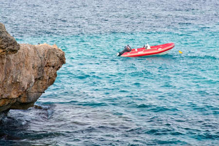 CALA RATJADA, MALLORCA, BALEARIC ISLANDS, SPAIN - JULY 14, 2014: Small moored red lifeboat and rock on July 14, 2014 in Cala Ratjada, Mallorca, Balearic islands, Spain.のeditorial素材