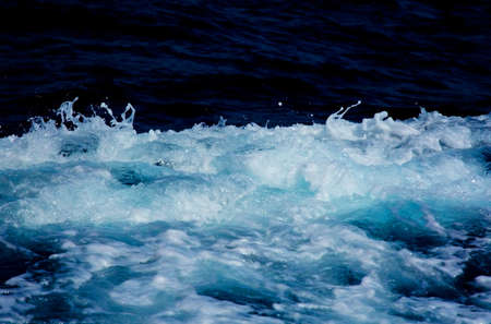 Azure and white boat wake sea foam with white splashes, sprays and drops on dark blue abstract