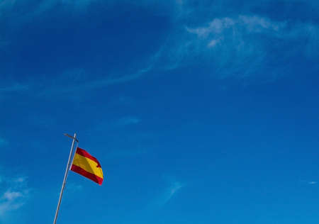 Spanish flag flying against blue sky in lower left corner with copy space.のeditorial素材