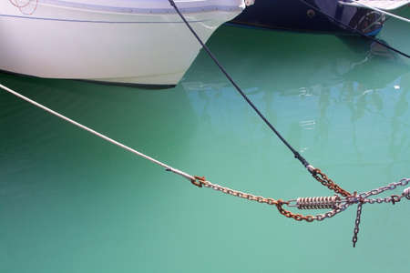 Detail of mooring rope, green water and white sailboat in marina.の写真素材