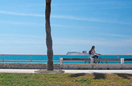 PALMA DE MALLORCA, SPAIN - APRIL 20, 2015: Woman riding a bike along the Paseo Maritimo and large ferry in the background on a sunny spring day on April 20, 2015 in Palma de Mallorca, Balearic islands, Spain.のeditorial素材