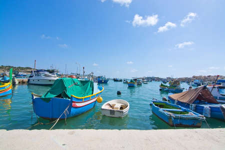 MARSAXLOKK, MALTA - SEPTEMBER 15, 2015: Colorful painted small boats moored in the clear turquoise water on a sunny day on September 15, 2015 in Marsaxlokk, Malta.のeditorial素材