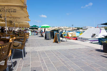 MARSAXLOKK, MALTA - SEPTEMBER 15, 2015: Marsaxlokk restaurant pier with parasols and signs on a sunny day on September 15, 2015 in Marsaxlokk, Malta.のeditorial素材