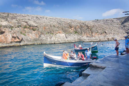 BLUE GROTTO, MALTA - SEPTEMBER 15, 2015: Pier with tourists and boats ready to go on tour in popular tourist attraction Blue Grotto on a sunny day in September 15, 2015 in Malta.のeditorial素材