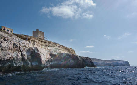 BLUE GROTTO, MALTA - SEPTEMBER 15, 2015: Limestone rocks with caves and clear turquoise water and people on top of cliff in Blue Grotto on a sunny day in September in Malta.のeditorial素材