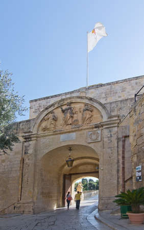 MDINA, MALTA - SEPTEMBER 15, 2015: Arched entrance portal with flag, people coming through and old city walls on a sunny day in September 14, 2015 in Mdina, Malta.のeditorial素材