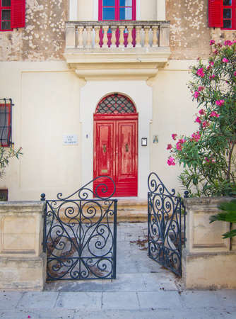 MDINA, MALTA - SEPTEMBER 15, 2015: Beautiful residential building inside Mdina wall with red doors, balcony, window shutters and entrance in black wrought iron on a sunny day in September 14, 2015 in Mdina, Malta.のeditorial素材