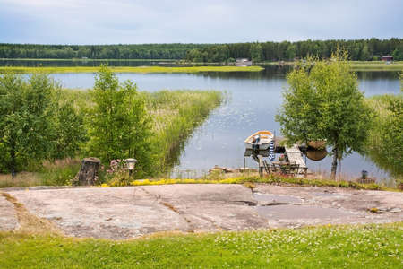 VARMLAND, SWEDEN - JUNE 20, 2014: Small boat moored by the jetty in inlet by the lake on a sunny summer evening on June 20, 2014 in Varmland, Sweden.のeditorial素材