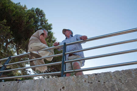 PORTO CRISTO, MALLORCA, SPAIN - JULY 2, 2011: Two men on a fence enjoy an outdoor chat on a sunny summer evening on July 2, 2011 in Mallorca, Balearic islands, Spain.のeditorial素材
