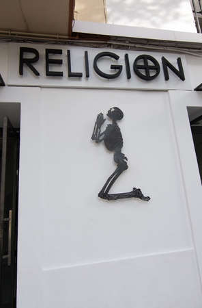 IBIZA, BALEARIC ISLANDS, SPAIN - DECEMBER 15, 2015: Skeleton figure praying and the word 'RELIGION' in block letters on a wall on December 15, 2015 in Ibiza town, Balearic islands, Spainのeditorial素材