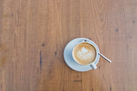 White cup with foaming cappuccino coffee and spoon