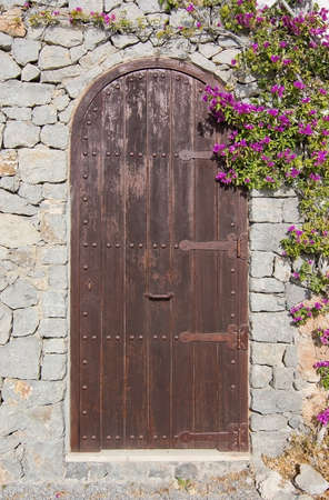 Brown wooden portal door with pink blossoming bougainvillea in Ibiza, Balearic islands, Spain on a sunny day in December.の写真素材
