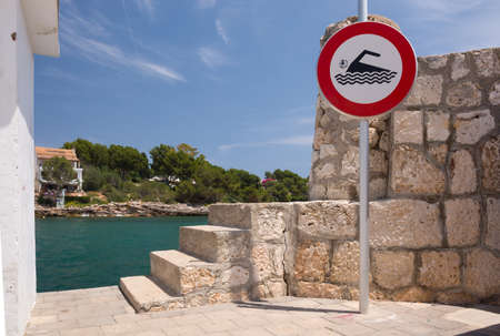 PORTO PETRO, MAJORCA, BALEARIC ISLANDS, SPAIN - JULY 21, 2013: Seaside stone stairs on quay and warning sign on a sunny summer day on July 21, 2013 in Aucanada, Balearic islands, Spain.のeditorial素材