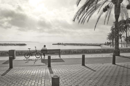 CAN PASTILLA, MALLORCA, BALEARIC ISLANDS, SPAIN - DECEMBER 14, 2015: Man rests on a bench in stark sunshine monochrome sepia image on December 14, 2015 in Mallorca, Balearic islands, Spainのeditorial素材