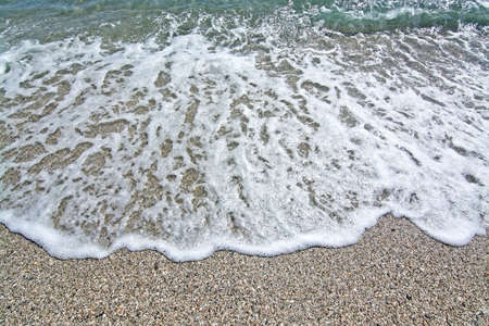 Foamy wave hits rocks and seashells beach closeup in Mallorca, Balearic islands, Spain.