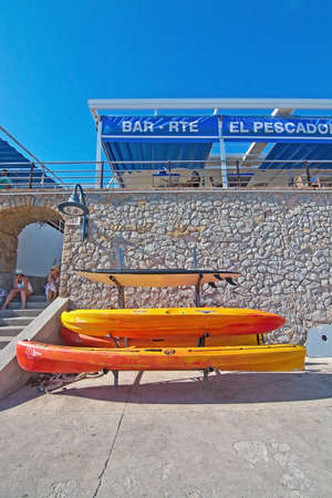 SANT ELM, MALLORCA, SPAIN - AUGUST 5, 2016: Stacked plastic canoes and El Pescador restaurant on the pier on a sunny summer day in August 5 in Sant Elm, Mallorca, Spain.のeditorial素材