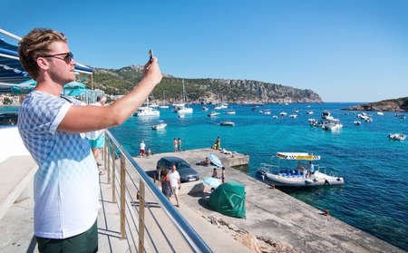 SANT ELM, BALEARIC ISLANDS, SPAIN - JULY 10, 2016: Young man taking photo with smartphone in Sant...