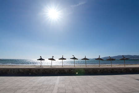 Parasols and sun on sandy beach with blue sky, Mallorca, Spain.の写真素材
