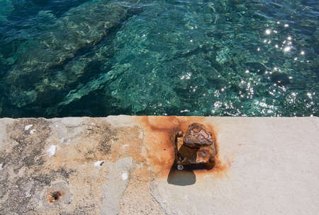 Rusty mooring knob on concrete pier and clear green water background textureの写真素材