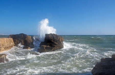 Windy day on the coast with splashing waves and sunshine .