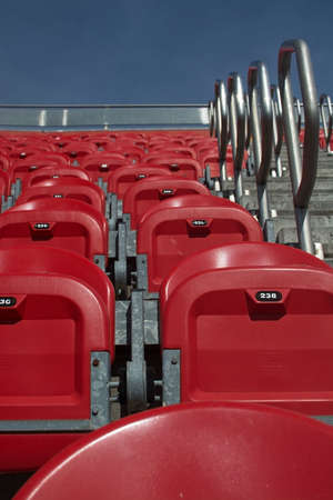 Red plastic seats at a soccer stadium closeup upwards in sunshine.のeditorial素材