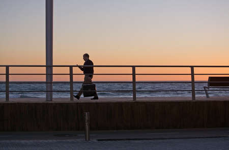 PALMA DE MALLORCA, SPAIN - JANUARY 4, 2018: Man walks home from work watching his smartphone in Molinar at dusk on January 4, 2018 in Palma de Mallorca, Spain.のeditorial素材