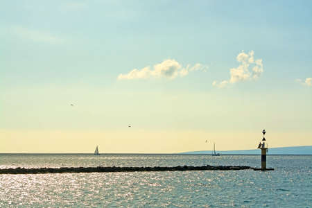 Maritime inlet with birds, ocean, horizon, pier and sailboat in Mallorca, Balearic islands, Spainの写真素材