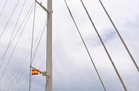 Spanish flag in mast of large sailing yacht against overcast sky in Mallorca, Spain.の写真素材