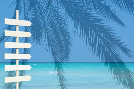 White wooden arrow signpost over blue ocean palm landscape turquoise water and horizonの写真素材