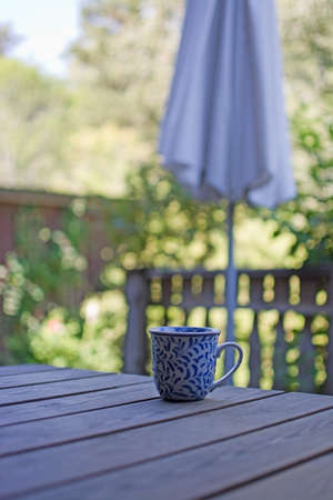 Mug in blue pattern on wooden table outdoors in the shade in a garden.の写真素材