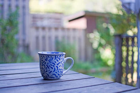 Mug in blue pattern on wooden table outdoors in the shade in a garden.の写真素材