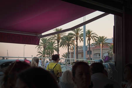 PALMA DE MALLORCA, SPAIN - JUNE 23, 2018: Terrace view at sunset with palms and people from the interior in a bar on June 23, 2018 in Palma de Mallorca, Spain.のeditorial素材