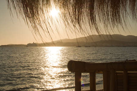 Sunset glittering water silhouettes through beach straw parasols in Palma de Mallorca, Spainの写真素材