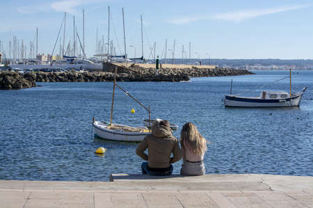PALMA DE MALLORCA, SPAIN - DECEMBER 6, 2018: Young couple sit on the  Cala Estancia pier on a sunny day on December 6, 2018 in Palma de Mallorca, Spain.のeditorial素材
