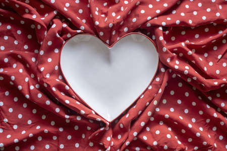 Stoneware heart shaped plate with red edge on red and white polka dot printed fabric fun romantic background texture.の写真素材