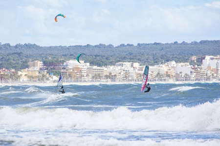 CAN PASTILLA, MALLORCA, SPAIN - APRIL 6, 2019: Surfers play in the green waves on a windy and sunny...