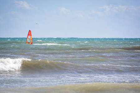 CAN PASTILLA, MALLORCA, SPAIN - APRIL 6, 2019: Windsurfer with red sail plays in the green waves on...