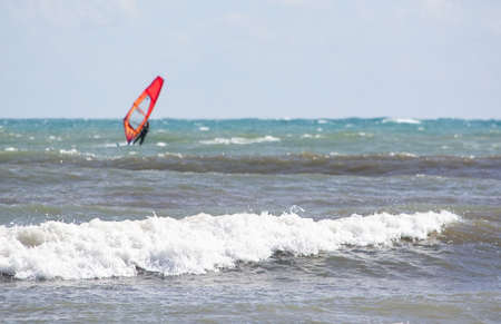 CAN PASTILLA, MALLORCA, SPAIN - APRIL 6, 2019: Windsurfer with red sail plays in the green waves on...