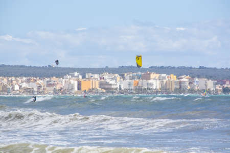 CAN PASTILLA, MALLORCA, SPAIN - APRIL 6, 2019: Surfers play in the green waves on a windy and sunny day on April 6, 2019 in Can Pastilla, Mallorca, Spain.のeditorial素材