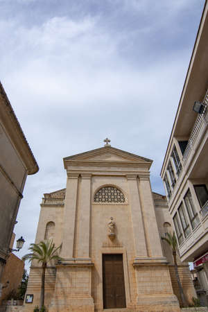 SES SALINES, MALLORCA, SPAIN - APRIL 15, 2019: Church built in neoclassical style in 1912 and street view in central city on an overcast day in the beginning of tourist season on April 15, 2019 in Ses Salines, Mallorca, Spain.のeditorial素材