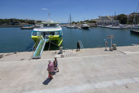 PORTO CRISTO, MALLORCA, SPAIN - MAY 16, 2019: Handiman paints in harbor area with moored catamaran and expensive yachts on a sunny day on May 16, 2019 in Porto Cristo, Mallorca, Spain.のeditorial素材