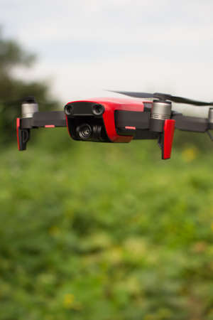 Small sized red drone is hovering in the air with green plants in the backgrtoundの写真素材