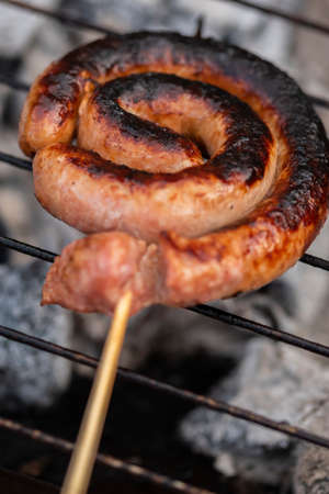 Close up shot of rolled up sausages on skewer placed over barbequeの写真素材