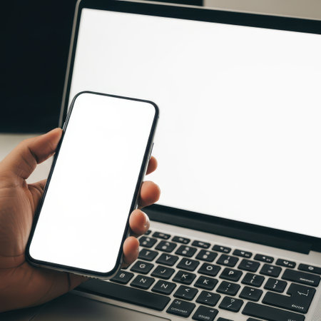 The image features a hand holding a smartphone near a laptop. The smartphone screen is blank, and the laptop screen is also blank. The image is on a transparent background, making it suitable for various digital applications. The focus is on the interaction between the smartphone and the laptop, highlighting technology and connectivity.の素材