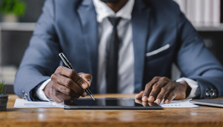 Close-up of African American businessman using digital tablet and making notes while sitting at his working placeの素材