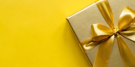 Gift box with gold ribbon on yellow background. Top view.の素材