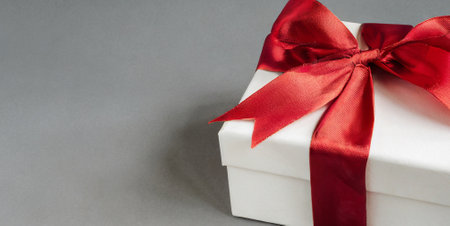White gift box with red ribbon bow on grey background. Copy space.の素材