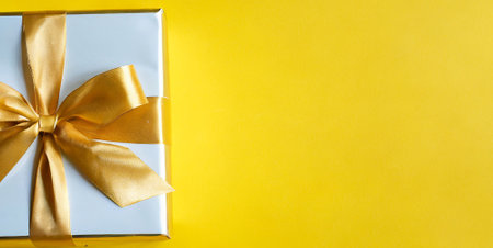 Gift box with golden ribbon on yellow background. Top view.の素材