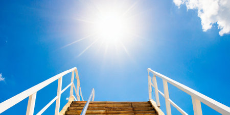 Wooden stairs leading to the blue sky with white clouds and sunの素材