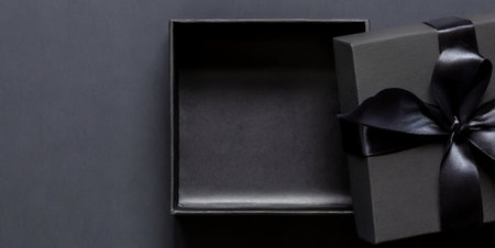 Black gift box with black ribbon on black background. Top view.の素材